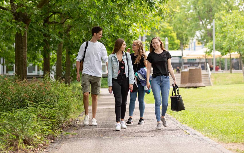 Studierende unterhalten sich während sie einen Weg auf dem grünen Campus entlang gehen