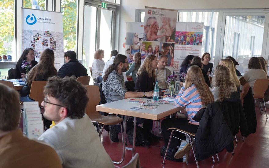 Studierende und Fachkräfte sitzen an Tischen in der Mensa und sind im Gespräch