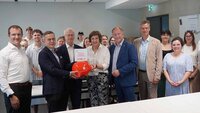 Gruppe von 7 Personen mit Sparschwein und Studierenden dazwischen und dahinter