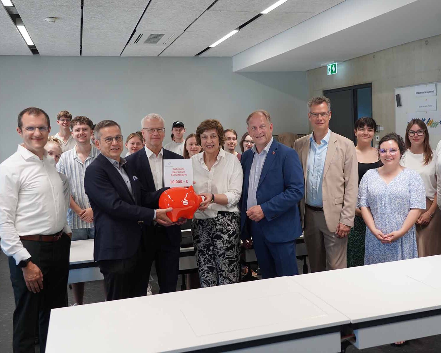 Gruppe von 7 Personen mit Sparschwein und Studierenden dazwischen und dahinter