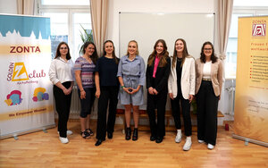 Sieben junge Frauen in einer Reihe, lächeln in die Kamera, rechts und links von ihnen Zonta-Roll-Ups