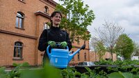 Eine junge Frau, die den Hochschulgarten gießt