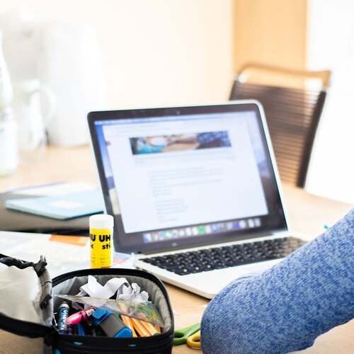 Schülerin arbeitet mit Mäppchen und Laptop an einem Tisch