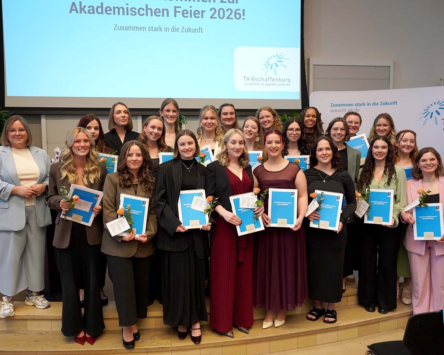 Gruppenbild der 23 Absolventinnen mit Urkunden und je einer Rose in der Hand zusammen mit Dekanin in der Aula