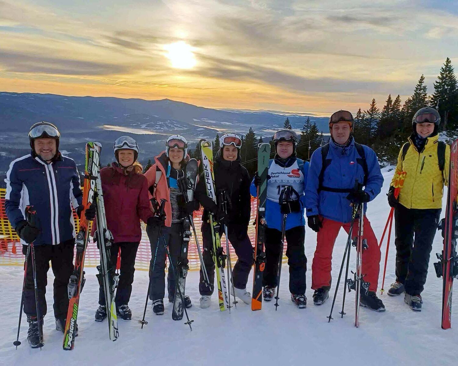 Sieben Personen stehen in Skiausrüstung mit Ski in der Hand auf der Piste. 