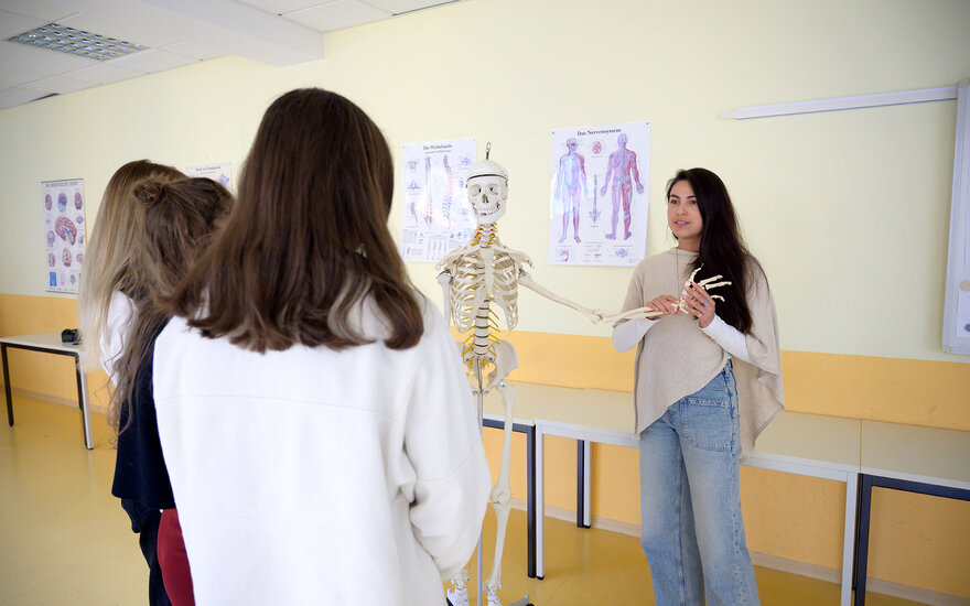 Schülerin erklärt ihren Mitschülerinnen Ausbildungsinhalte mithilfe eines Skeletts