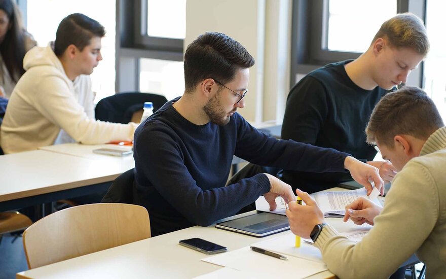 Drei Studenten sitzen gemeinsam am Tisch und bearbeiten die Workshop-Aufgaben.