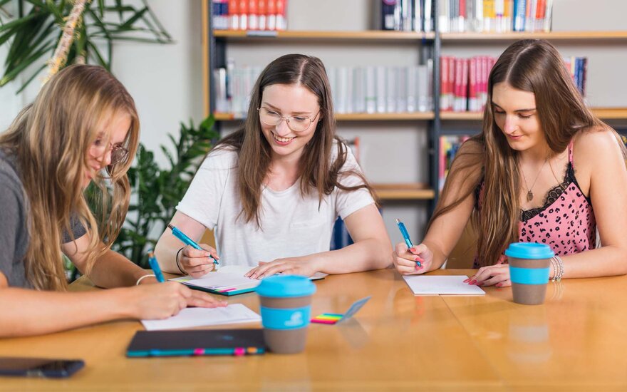 Drei Studentinnen während Gruppenarbeit in der Bibliothek