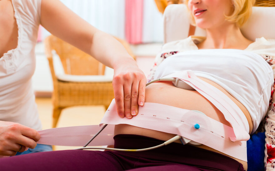 Anlegen eines CTG Gurts um den Bauch einer Schwangeren