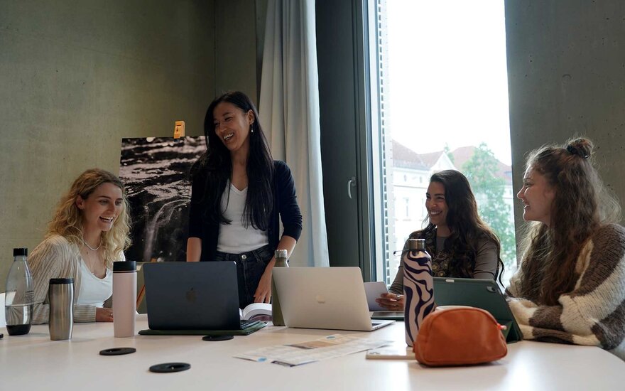 Vier Studentinnen lachen bei einer Gruppenarbeit.