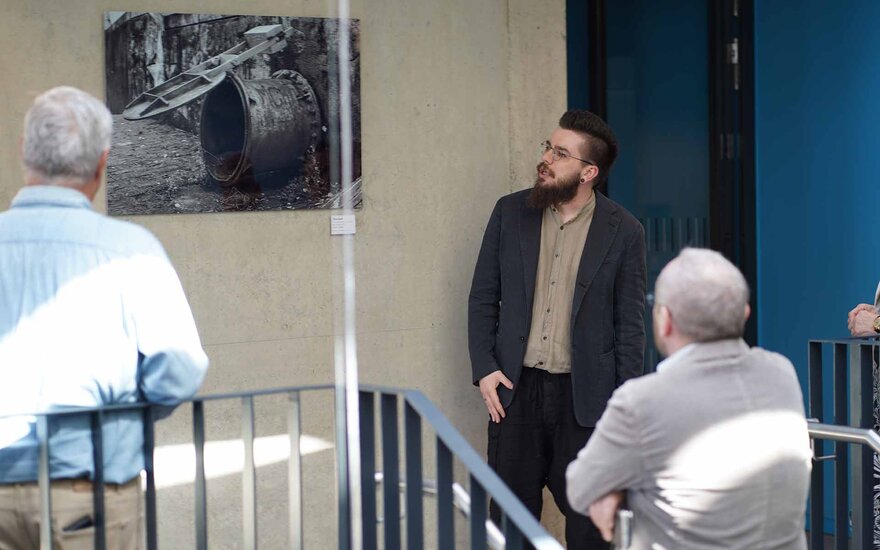 Der Künstler steht mit zwei älteren Männern vor einem Bild an der Treppe