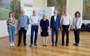 Eine Gruppe von sieben Personen stehen in einer Reihe lächelnd in einem Saal. Im Hintergrund das Logo der TH Aschaffenburg auf einer Messewand.