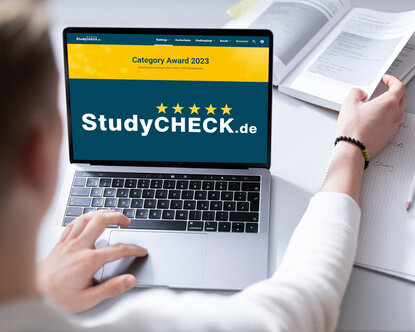 Ein Student sitzt vor einem Laptop, auf dem die Website und das Logo von StudyCheck zu sehen ist