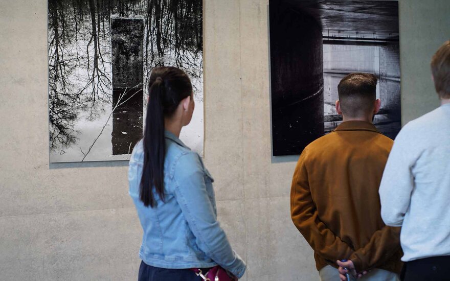 Eine Frau und zwei Männer betrachten die Bilder an der Wand.