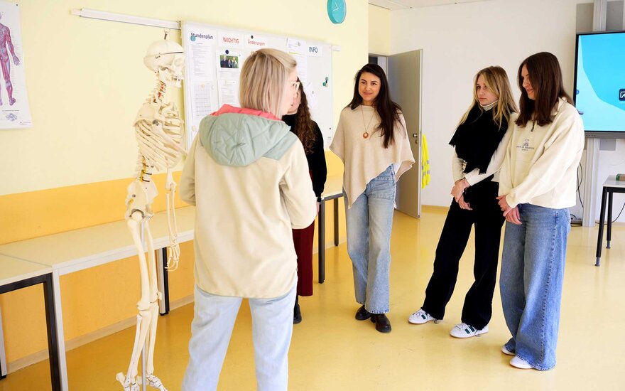 Lehrkraft erklärt vier Auszubildenden Lehrinhalte der Ergotherapie.