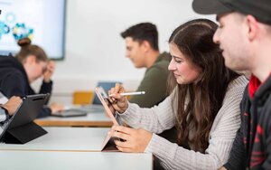 Vier Studierende sitzen nebeneinander an Tischen und arbeiten an Tablets