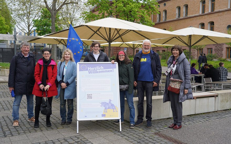 Gruppenfoto und Europaflagge auf dem Campus vor Mensagelände mit Sonnenschirmen