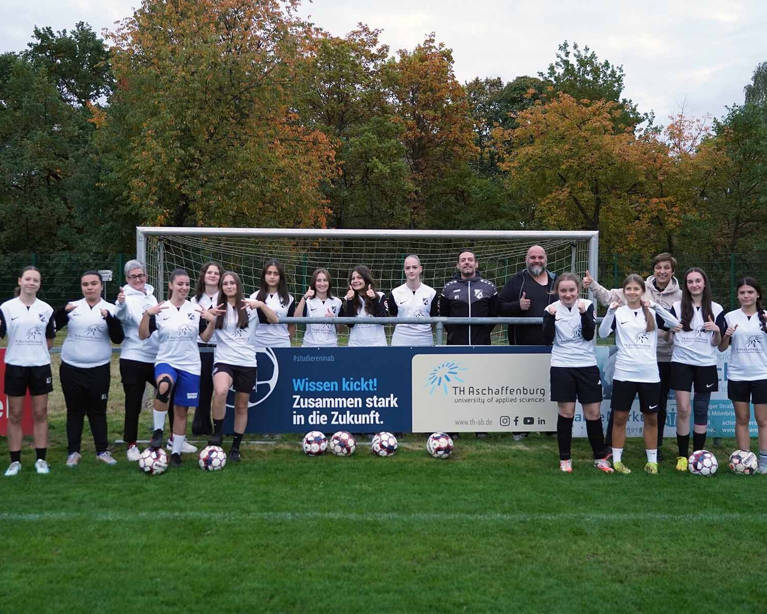Fußballmannschaf mit Trainern steht vor Bandenwerbung und Tor auf dem Fußballplatz
