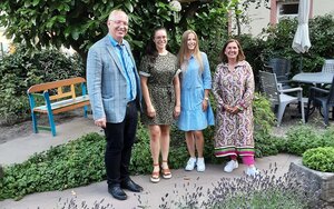 Zwei junge Frauen in Sommerkleidern stehen in einem Garten mit einem Professor und einer Frau mittleren Alters