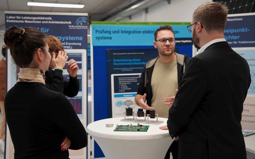 Vier Menschen unterhalten sich an einem Messestand. Im Hintergrund befinden sich Roll-ups. 