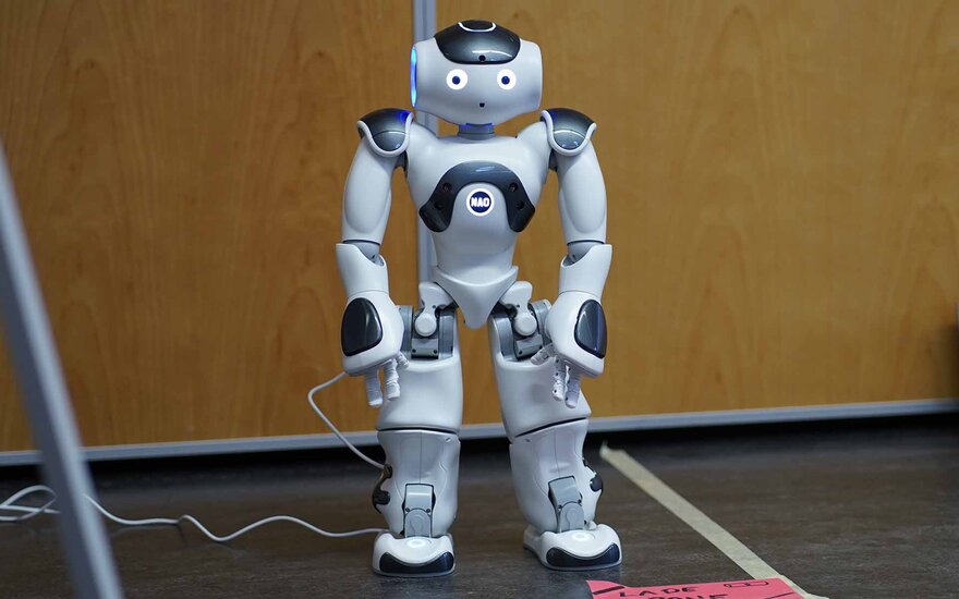 Stehender NAO-Roboter, der mit Armen, Beinen, einem Kopf und blau leuchtenden Augen sehr menschenähnlich wirkt