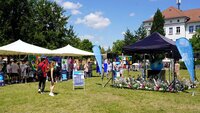 Campuswiese mit Menschen an Infoständen und weißen Zelten im Hintergrund sowie 30-Jahre-Keyvisual auf blau überdachter Bühne