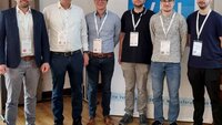 Der Tagungsleiter und fünf Studierende und Absolventen stehen nebeneinander vor einem blauen Plakat und lächeln in die Kamera
