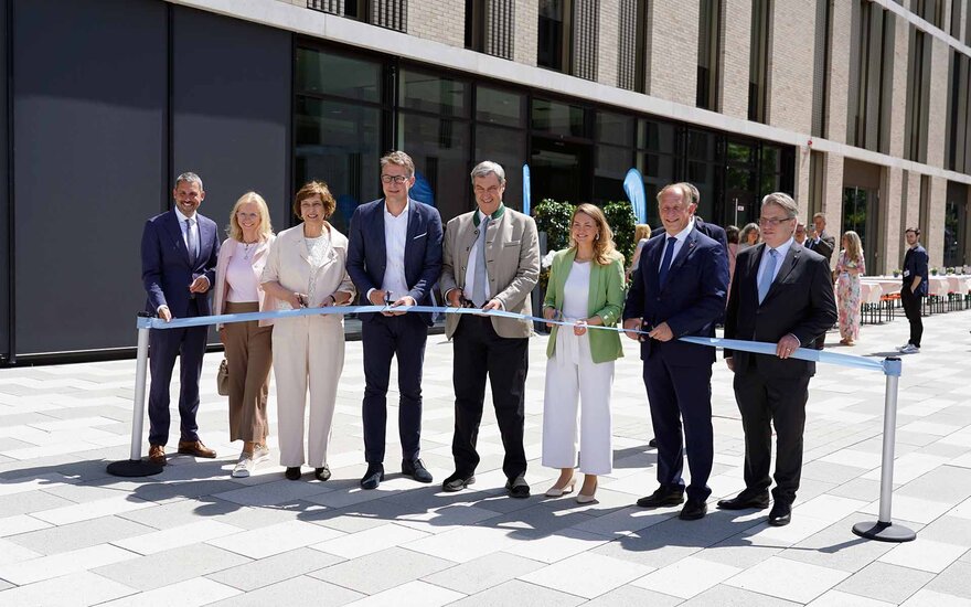 Acht Personen stehen vor dem Neubau hinter einem blauen Band, fünf von ihnen haben Scheren in der Hand