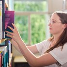 Studentin stellt Buch in Buchregal in der Bibliothek