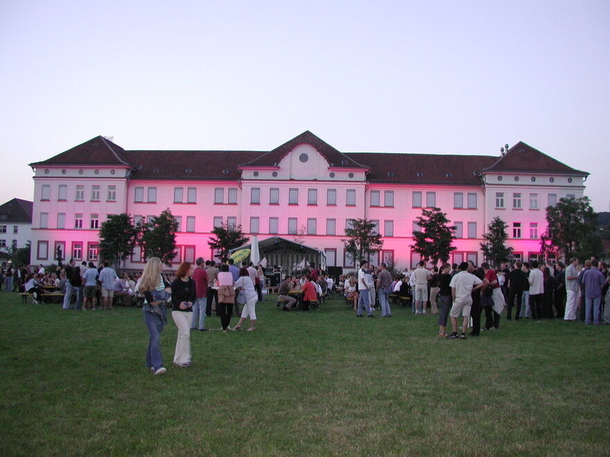 Viele Menschen sind am Abend auf der Campusiwese. Im Hintergrund ist ein Gebäude der Technischen Hochschule Aschaffenburg bunt beleuchtet.