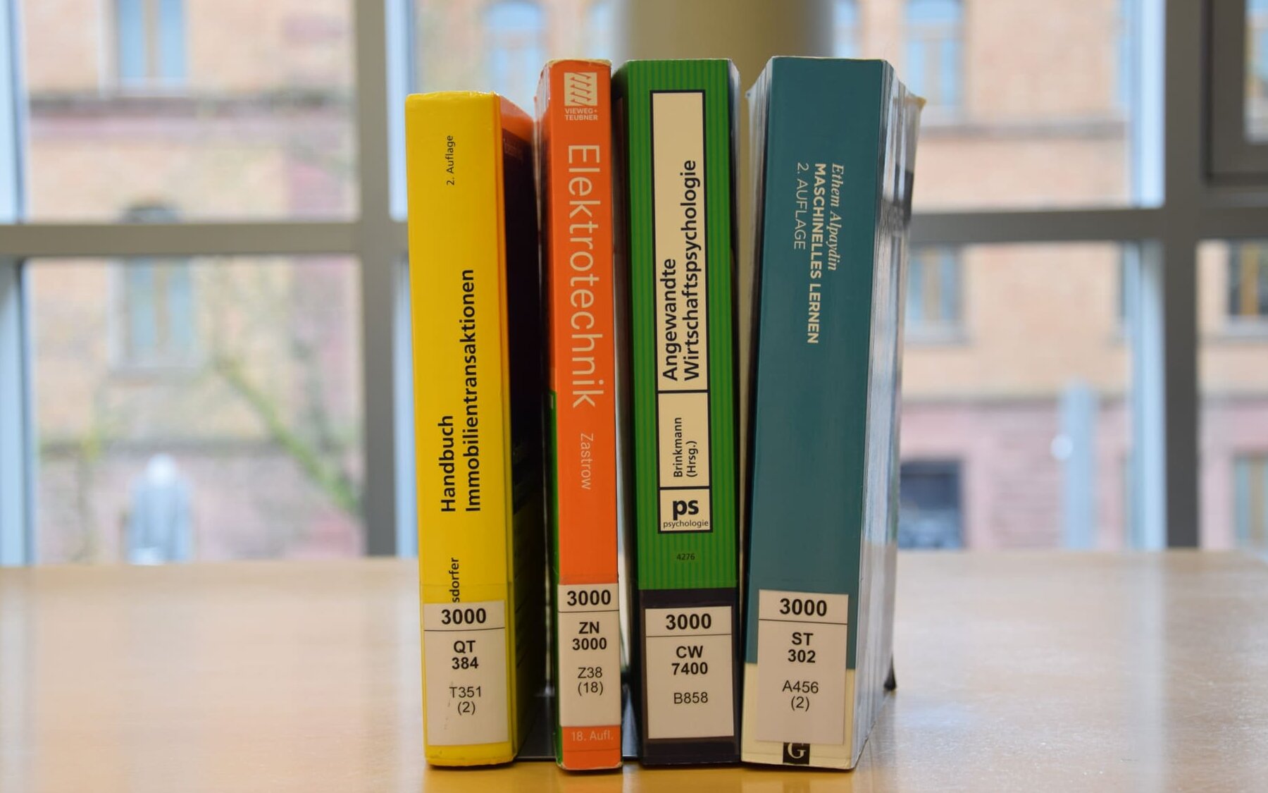 Vier farbige Bücher stehend auf Tisch in Bibliothek