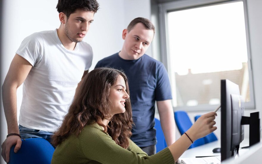 Drei Studierende aus dem Studiengang Software Design besprechen etwas an einem Desktop