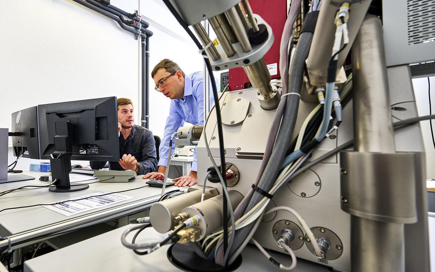 Zwei Mitarbeiter stehen hinter dem Rasterelektronenmikroskop des ZeWiS.