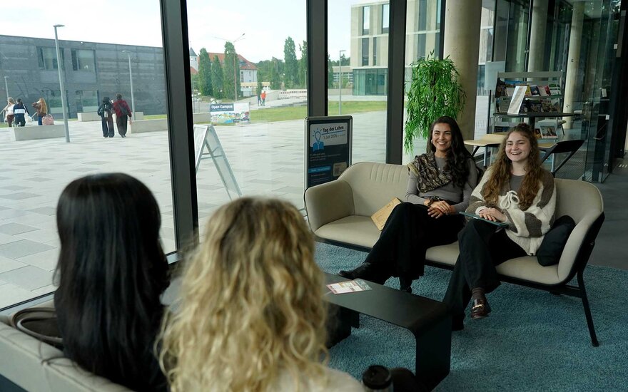 Vier Studentinnen sitzen auf zwei Bänken und unterhalten sich.