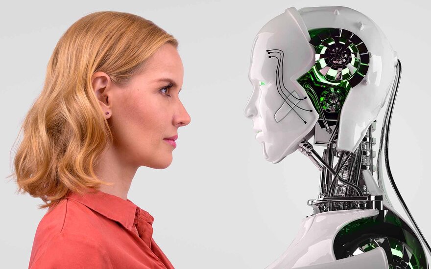 Eine blonde Frau steht einem weißen Roboter gegenüber, in dessen Kopf man die Technik sehen kann