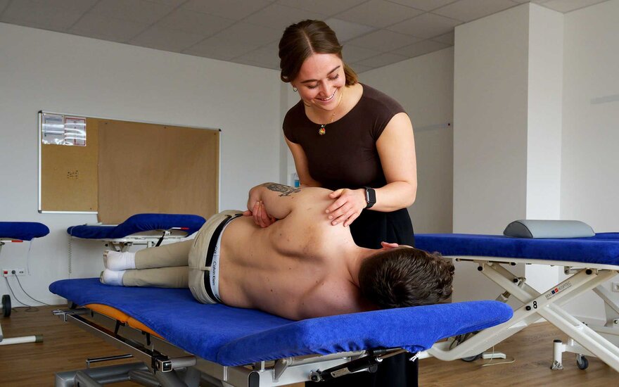 Frau bewegt den Arm und die Schulter von liegendem Patient in der Physiotherapie