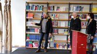 Künstler steht vor dem Bücherregal neben seiner Skulptur und erläutert seine Inspiration