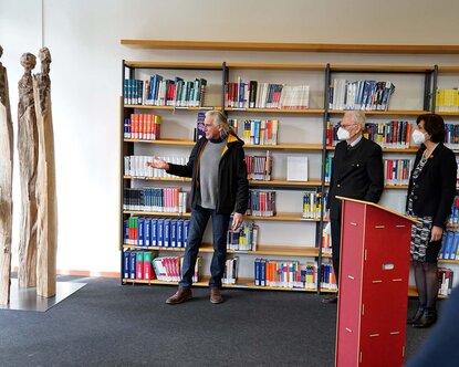 Künstler steht vor dem Bücherregal neben seiner Skulptur und erläutert seine Inspiration