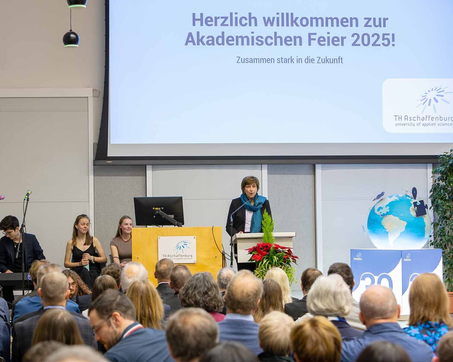 Publikum von hinten mit Blick auf Präsidentin am Rednerpult, Herzlich Willkommen auf Leinwand