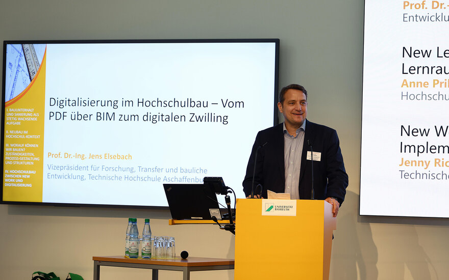 Mann hinter Rednerpult vor Präsentation