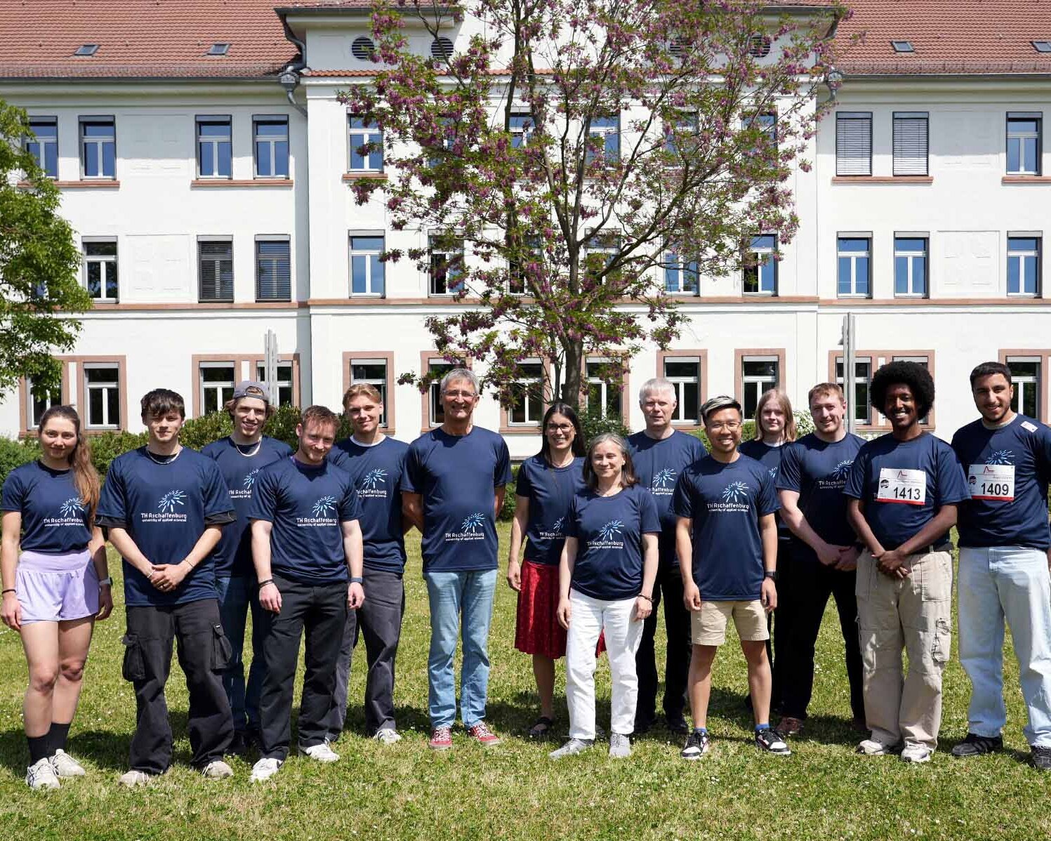 Laufteam der TH AB mit blauen T-Shirts auf Campuswiese vor weißem Gebäude 20
