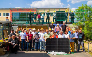 Gruppenfoto bei gutem Wetter vor und auf einem Gebäude einer Grundschule mit Photovoltaik-Anlage, viele Personen tragen Bauhelme