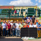 Gruppenfoto bei gutem Wetter vor und auf einem Gebäude einer Grundschule mit Photovoltaik-Anlage, viele Personen tragen Bauhelme