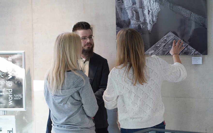Der Künstler steht mit zwei Frauen vor einem Bild und spricht mit ihnen