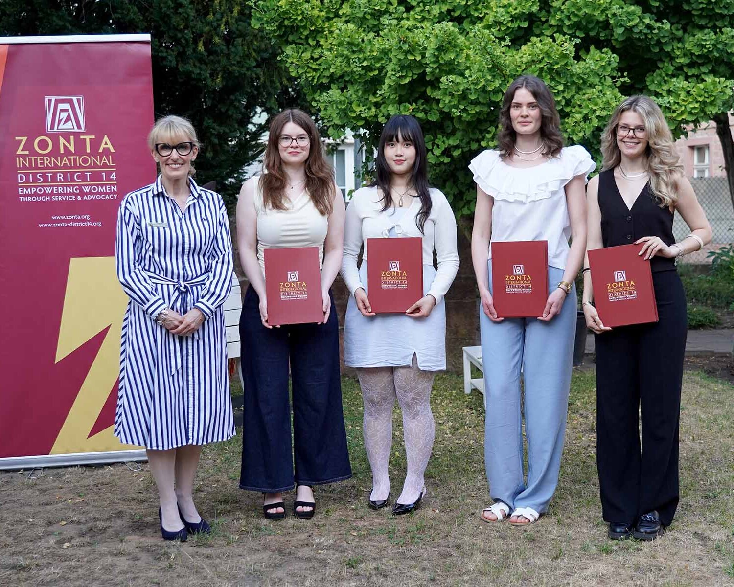 Zonta-Präsidentin mit den vier Preisträgerinnen mit Urkunden in der Hand vor Zonta-Roll-up