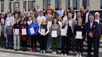 Gruppenbild mit rund 40 Personen, die teilweise Zertifikate halten, auf Treppenstufen vor den Neubauten