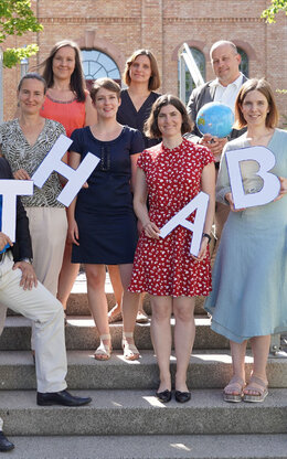 Gruppenfoto der Mitglieder des International Offices der TH AB, Personen stehen auf einer Steintreppe im Freien und halten Pappbuchstaben TH AB in der Hand.