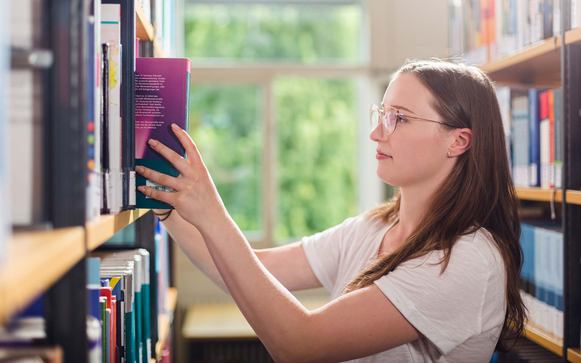 Studentin stellt Buch in Buchregal in der Bibliothek
