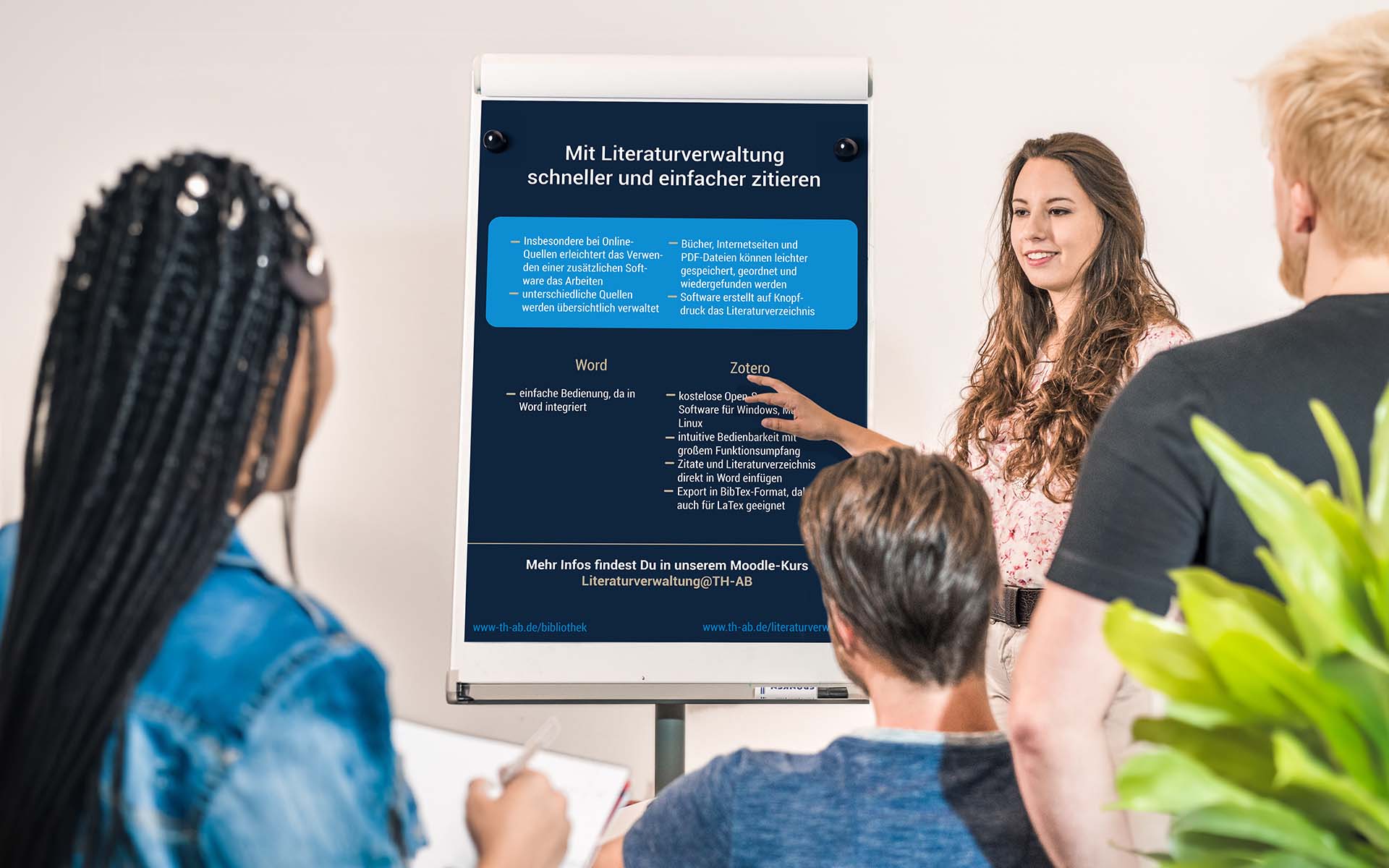 Drei Studierende hören einer Studierende, Referentin, Professorin, Dozentin zu, zeigt auf Flipchart mit Infos zum Zitieren