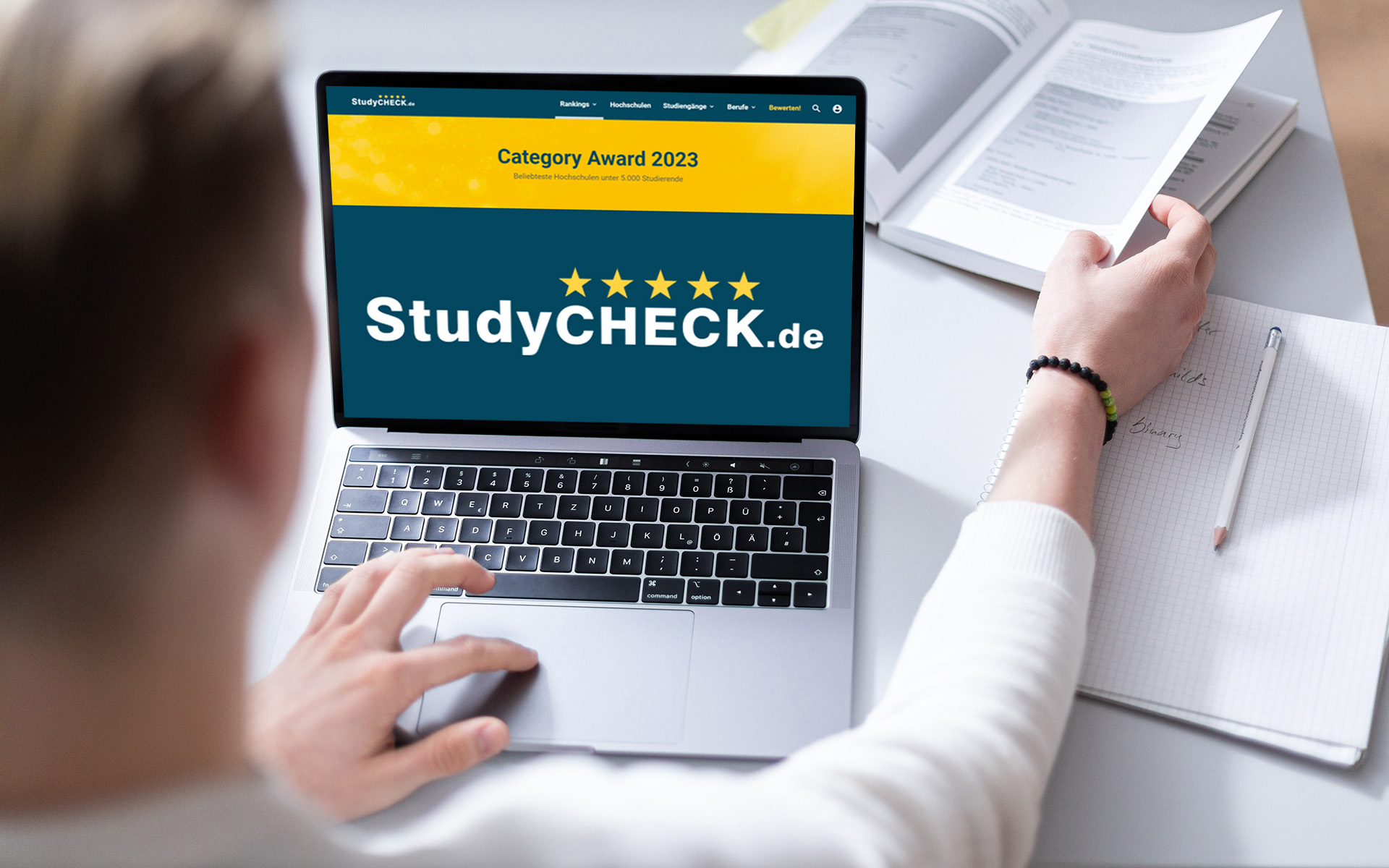 Ein Student sitzt vor einem Laptop, auf dem die Website und das Logo von StudyCheck zu sehen ist